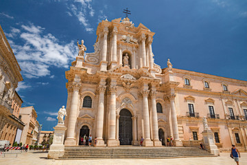 Some tourists are walking admiring the baroque cathedral in the historic center of the island of...