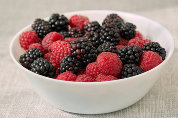 Close ip of a white bowl with ruspberries and blackberries.