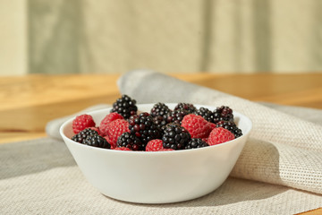 Close ip of a white bowl with ruspberries and blackberries.