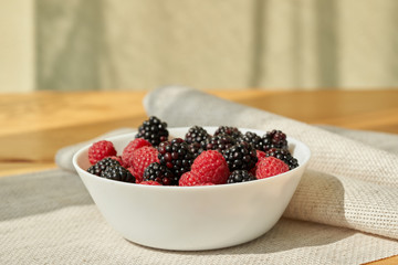 Close ip of a white bowl with ruspberries and blackberries.