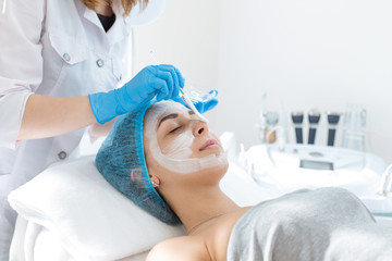 A professional cosmetologist applies a nourishing cream on the patient's face. Moisturizing, cleaning and facial skin care. Cosmetic procedures