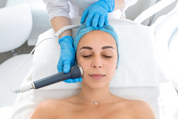 Obraz na płótnie Canvas Beautician procedure ultrasound fonoforeza patient face. A young girl is undergoing a course of spa treatments in the office of a beautician. Moisturizing, cleaning and facial skin care. procedures