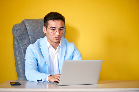 Asian Kazakh businessman in a suit and glasses with a laptop computer works in the office, a successful professional manager solves business issues