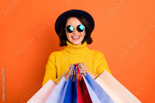 Photo of shopping cheerful girl wearing cap showing you what she has bought while isolated with orange background