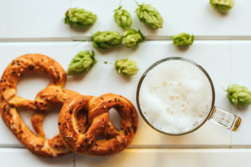  beer mug, hop cones and pretzels on a white wooden table. Oktoberfest background