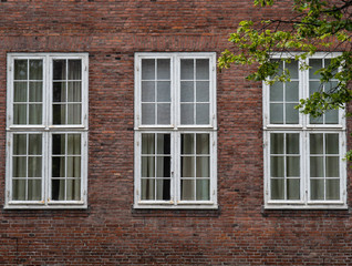 Three large rectangular windows with white metal bars on the facade of an old brick house