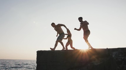Group of young friends jumping and doing tricks from a pier into the sea, super slow motion - Powered by Adobe