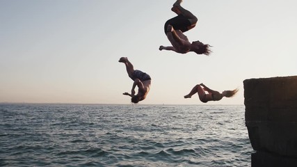 Group of young friends jumping and doing tricks from a pier into the sea, super slow motion