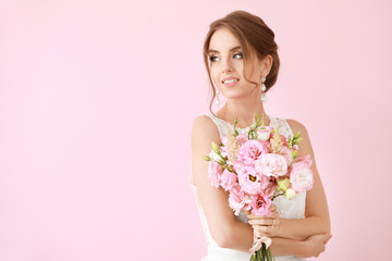 Portrait of beautiful young bride with wedding bouquet on color background