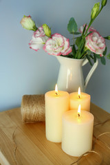 Fototapeta na wymiar Beautiful burning candles with threads and flowers in jug on wooden table