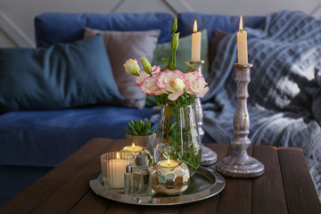 Beautiful burning candles with flowers on wooden table in room