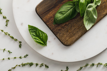 Top view of round marble surface with brown wooden cutting board and basil bundle near thyme twigs...