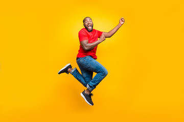 Fototapeta na wymiar Full length body size photo of black man wearing red t-shirt having caught something invisible and now dragging it while isolated with yellow vivid background