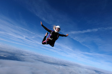 Naklejka na ściany i meble Skydiving. Blonde girl is flying in the blue sky.