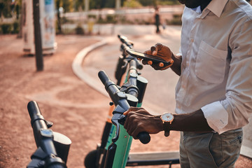 Young african guy is paying for electrical scooter by web payment using his mobile phone. © Fxquadro