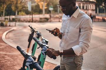 Young african guy is paying for electrical scooter by web payment using his mobile phone. © Fxquadro