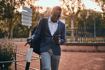 Attractive american tourist in sunglasses is paying for electrical scooter using his mobile phone.