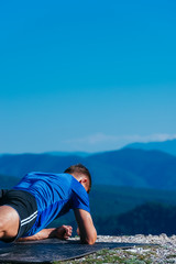 Strong male athlete doing plank while exercising his abs on top of a mountain on a sunny day.