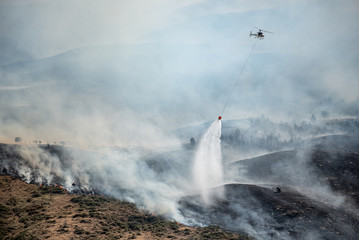 Firefighting helicopter with bucket drop water on forest fire or wildfire.