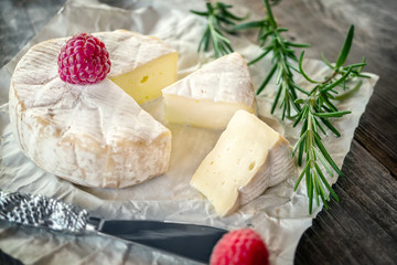 Delicatessen spicy Camembert cheese, brie with rosemary and raspberry on a beautiful textured wooden background. Spicy appetizer for gourmets. Selective focus