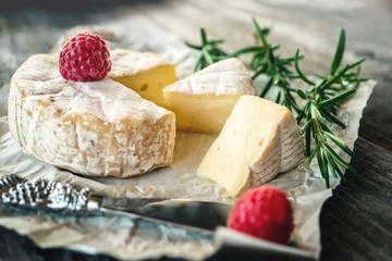 Fototapeta na wymiar Delicatessen spicy Camembert cheese, brie with rosemary and raspberry on a beautiful textured wooden background. Spicy appetizer for gourmets. Selective focus