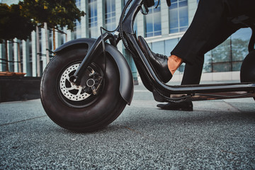 Elegant businessman in black suit is sitting on his electrical scooter near his office. © Fxquadro