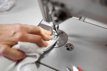 Obraz na płótnie Canvas Seamstress hand stitching white fabric on professional machine at workplace. Footplate of sewing machine holding fabric down onto the part that feeds it under needle. Close up view. Blurred background