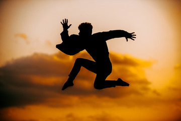 Fototapeta na wymiar Young silhouette man break dancing against sunset clouds background