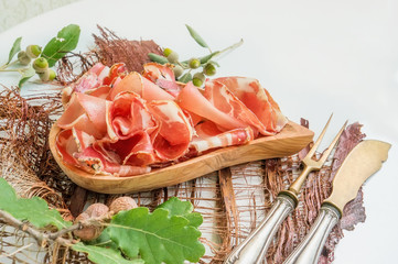 the aroma of ham and spices, thinly sliced on a white table with bread antique Cutlery and red wine