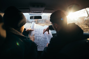 Two violent robbers sitting in a car looking at a blueprint of the building they want to rob while...