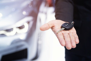 Business man hand holding car key front with car in showroom on background. transport dealership...