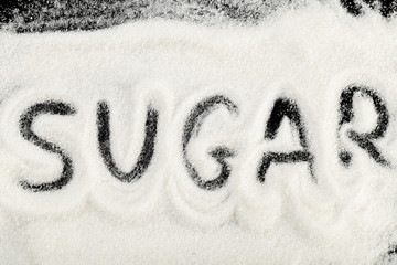 The word sugar written into a pile of white granulated sugar with a black background - Image
