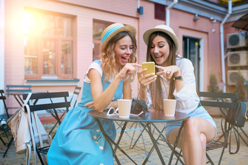 Two beautiful girls in hats with a smartphone in an outdoor cafe