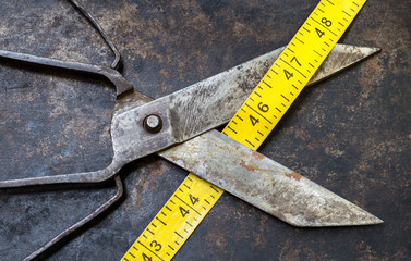 Weight loss, diet concept. Vintage sciccors with tape measure on a grunge metal background.
