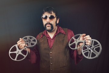 A man in vintage 1970's era clothing including big collars, leather vest, greasy mustache and...