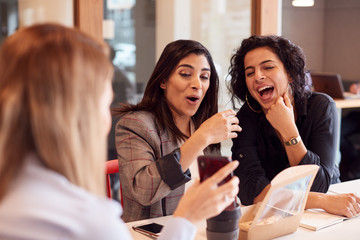 Group Of Young Businesswomen Sitting Around Table Having Working Lunch And Looking At Mobile Phones