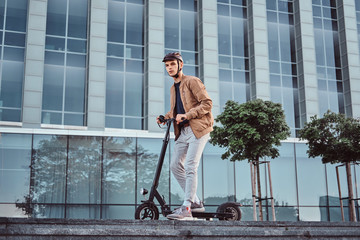 Young attractive student is driving his scooter neat interesting glass building at bright sunny day. © Fxquadro