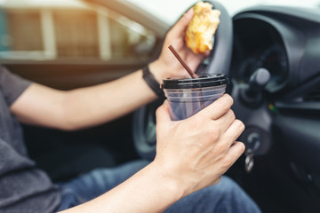 Man eating a pizza and holding coffee cup while driving car.