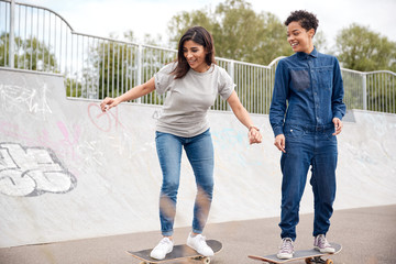 Two Female Friends Riding On Skateboards In Urban Skate Park