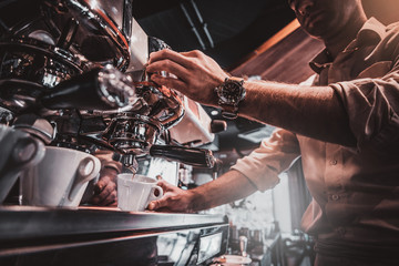 Talanted barista is prepairing coffee for clients at posh restaurant using coffee machine.