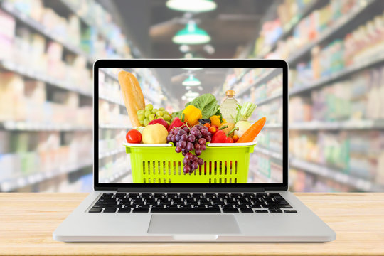 supermarket aisle blurred background with laptop computer and shopping basket on wood table grocery online concept