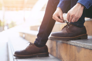 Businessman in a shirt jeans tie up shoelace on wearing brown leather shoes sitting staircase...