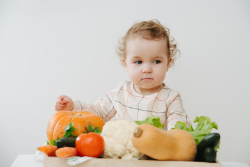 Little girl plays at the table with vegetables