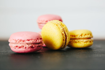 Sweet colorful French macaroon cookies dessert on black stone surface over white wooden background