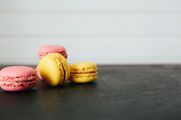 Sweet colorful French macaroon cookies dessert on black stone surface over white wooden background