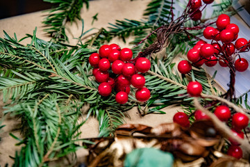 Red berries on a green background. Vibrant red artificial berries atop mess of green spruce branches on brown background. Traditional Christmas red and green decorations. Winter holiday backdrop. 