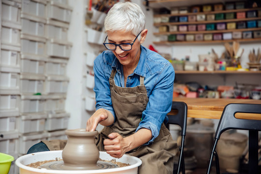 Senior female potter working on pottery wheel while sitting  in her workshop