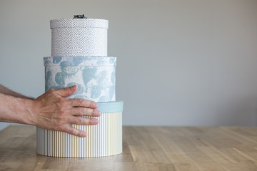 A stack of round gift boxes, standing on a wooden surface, is held by a person's hands.