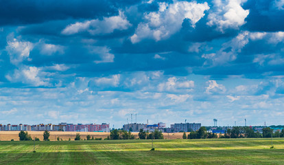White clouds in a blue sky above a field in the distance a city is visible ..