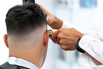 Barber cutting hair with a razor to a client in his barbershop